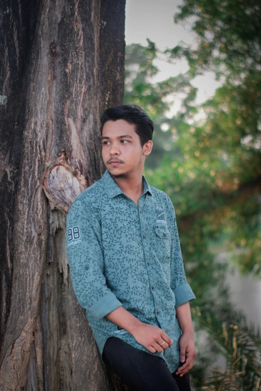 man wearing blue shirt leaning against tree