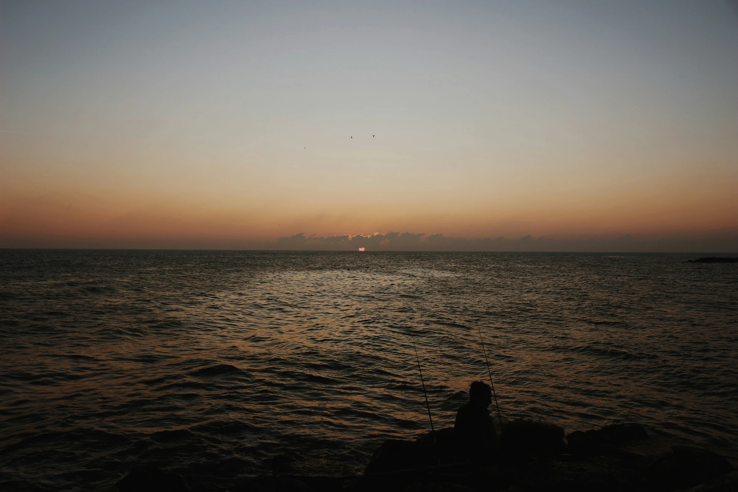 a person sitting in the middle of the water watching the sunset