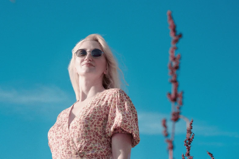 a woman wearing a dress standing in the sun with a clear blue sky behind her