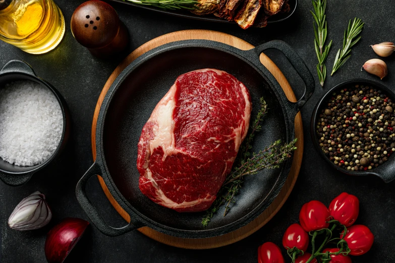 the steak is in a cast iron pan surrounded by spices, pepper and herbs