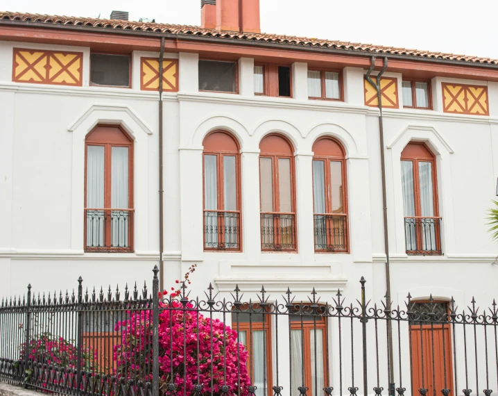 an image of a building with a metal gate and red flowers