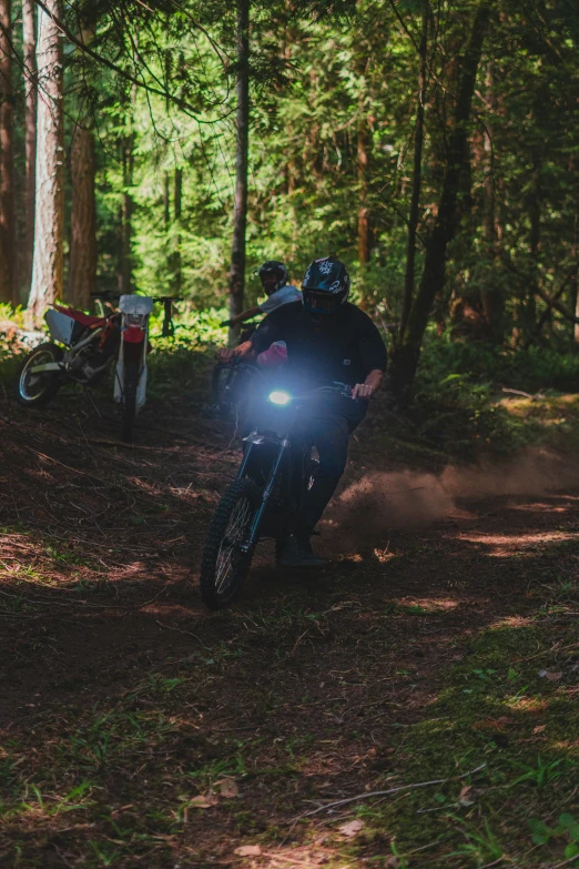 two people on motorbikes with headlights driving through the forest