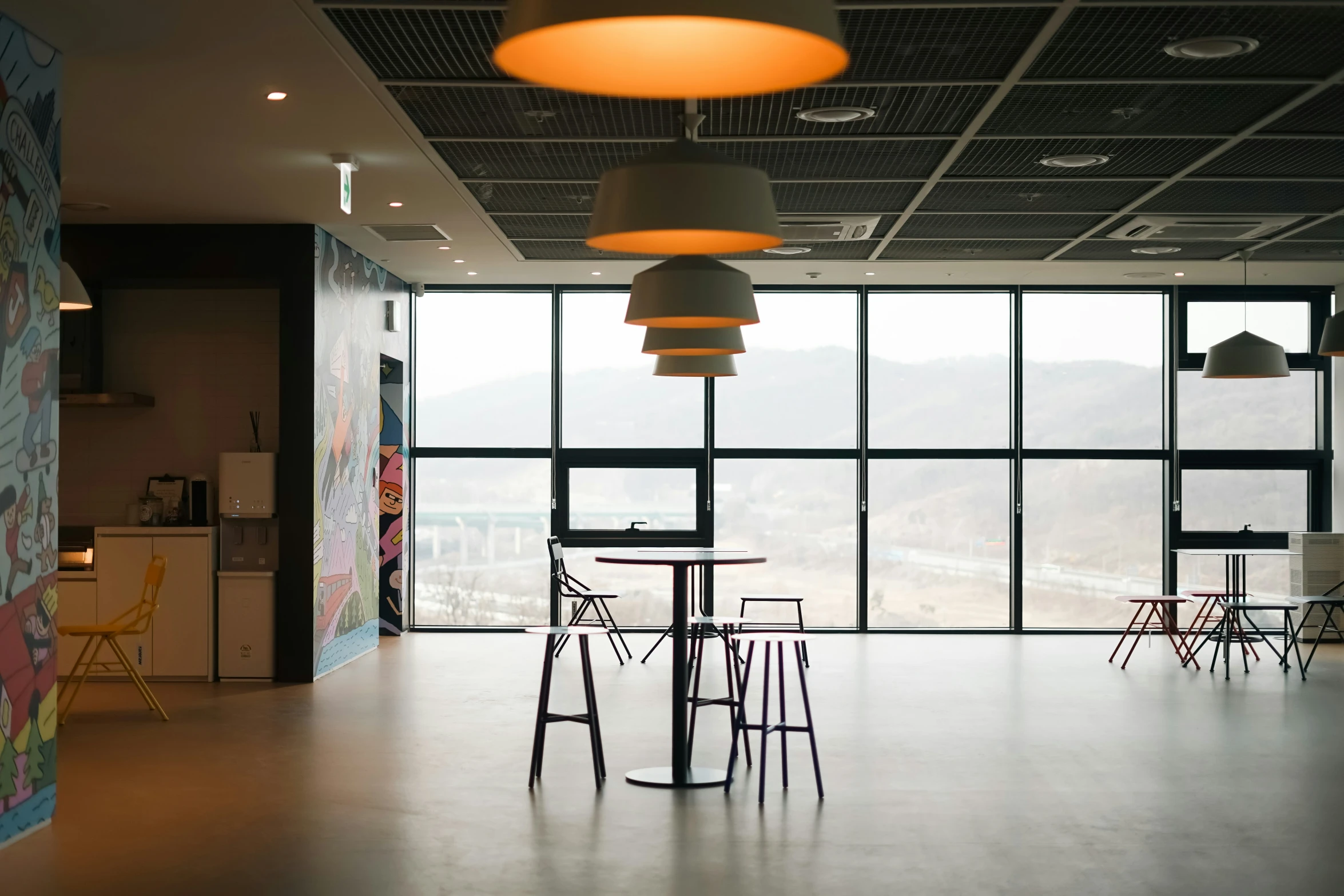 a table, chairs and some other items with big windows in the background