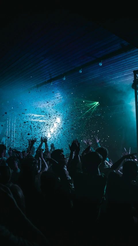 a crowd at a concert in the dark, many are holding their arms up