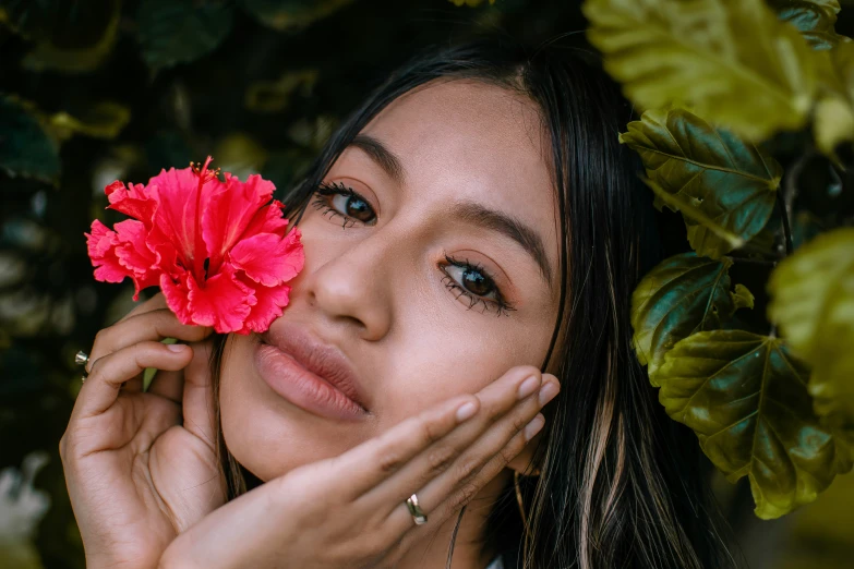 a young woman holding her hand near her face while holding a flower