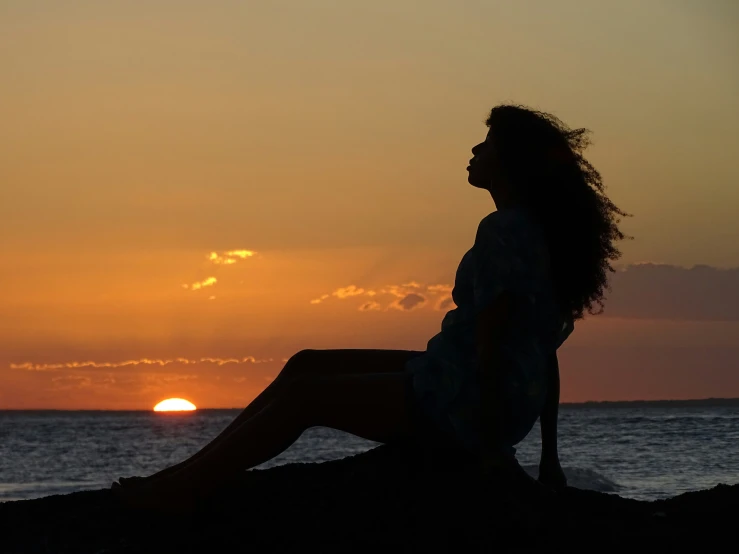 a person sitting in front of the sunset on a beach