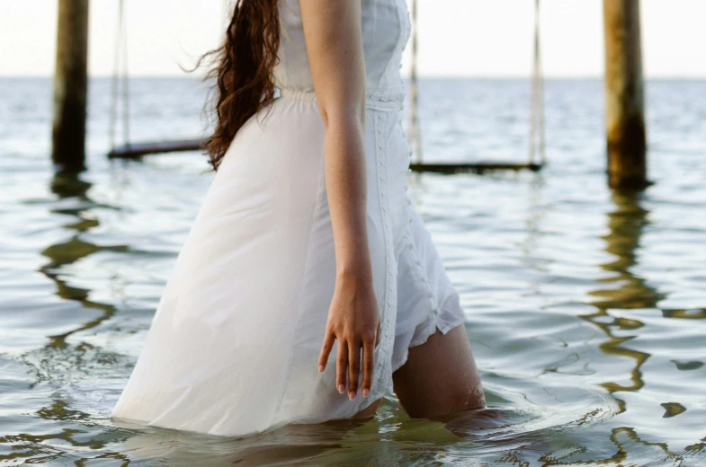 a woman in a long white dress wading through the water