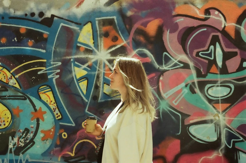a girl is walking in front of a wall covered with graffiti