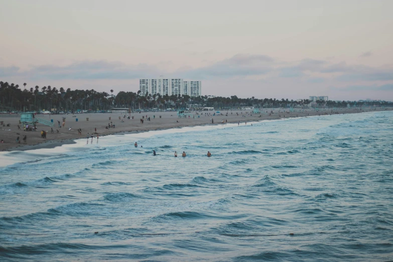 a very crowded beach with people on the beach and trees lining the hill