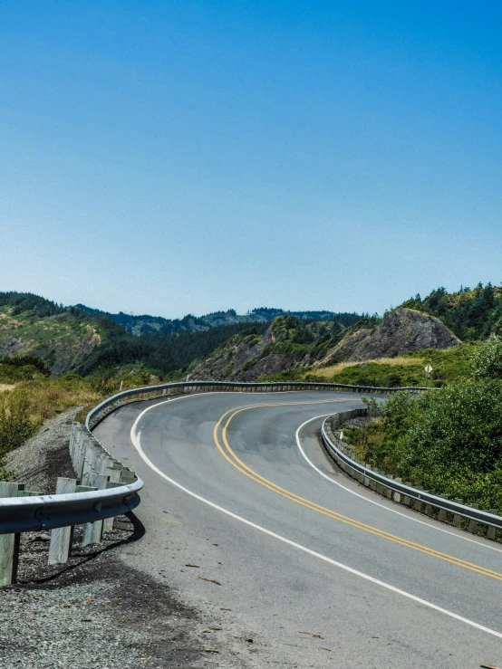 a curved road near a hillside and forest