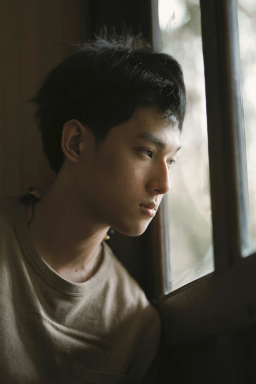 young man looking out of window with light from side