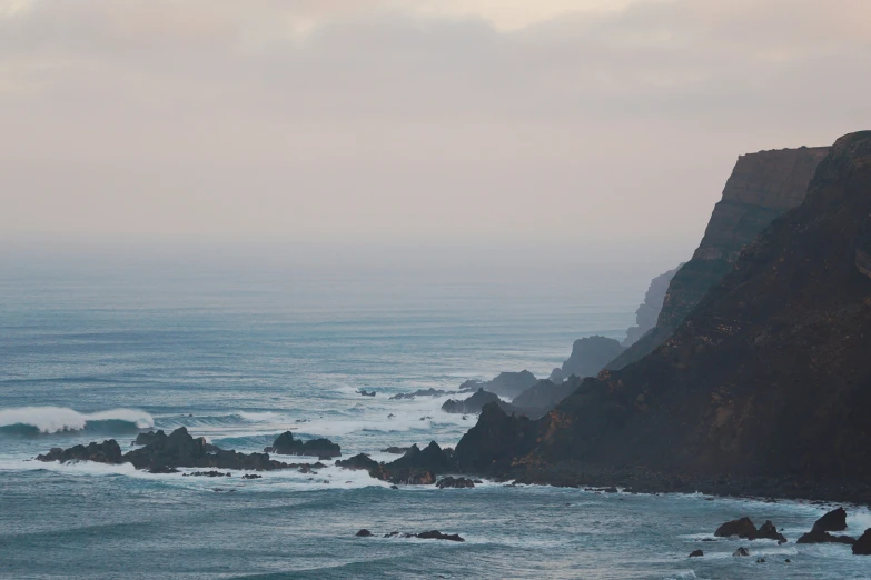 the ocean has waves coming in on the rocky shore