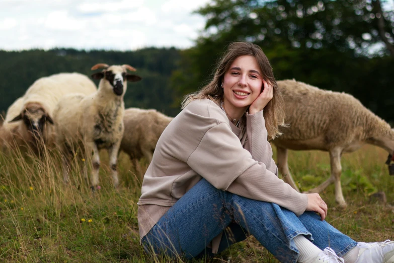 a young lady sitting on a field with sheep