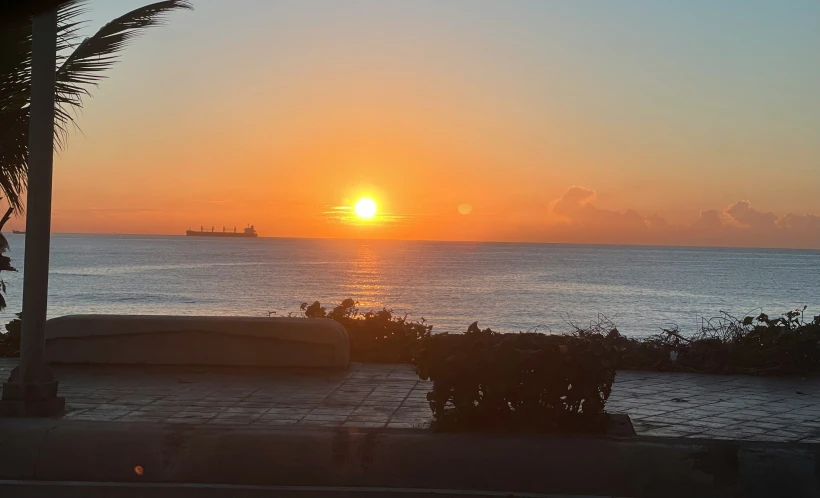 the sun rises over the ocean in front of a barge