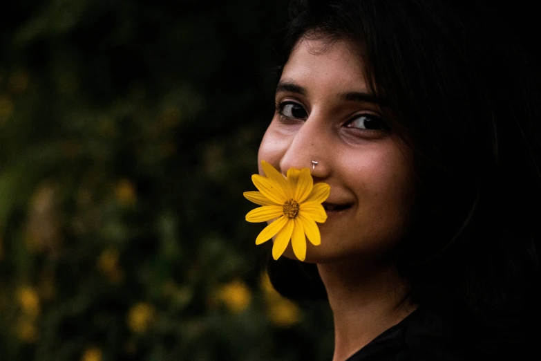 a woman with black hair and a yellow flower in her mouth