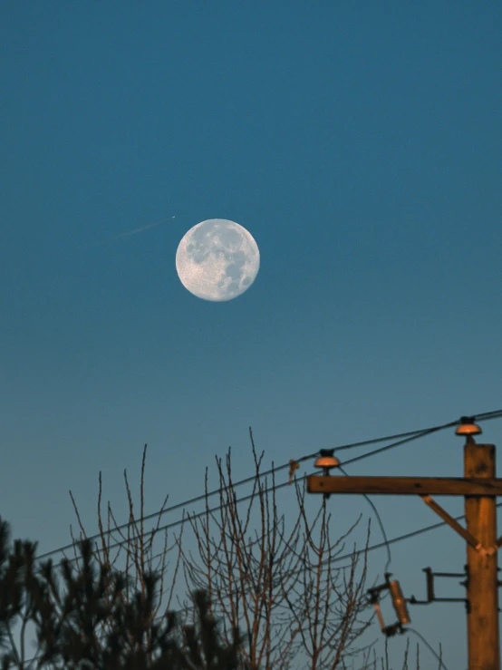 the full moon rising in the sky, surrounded by power lines