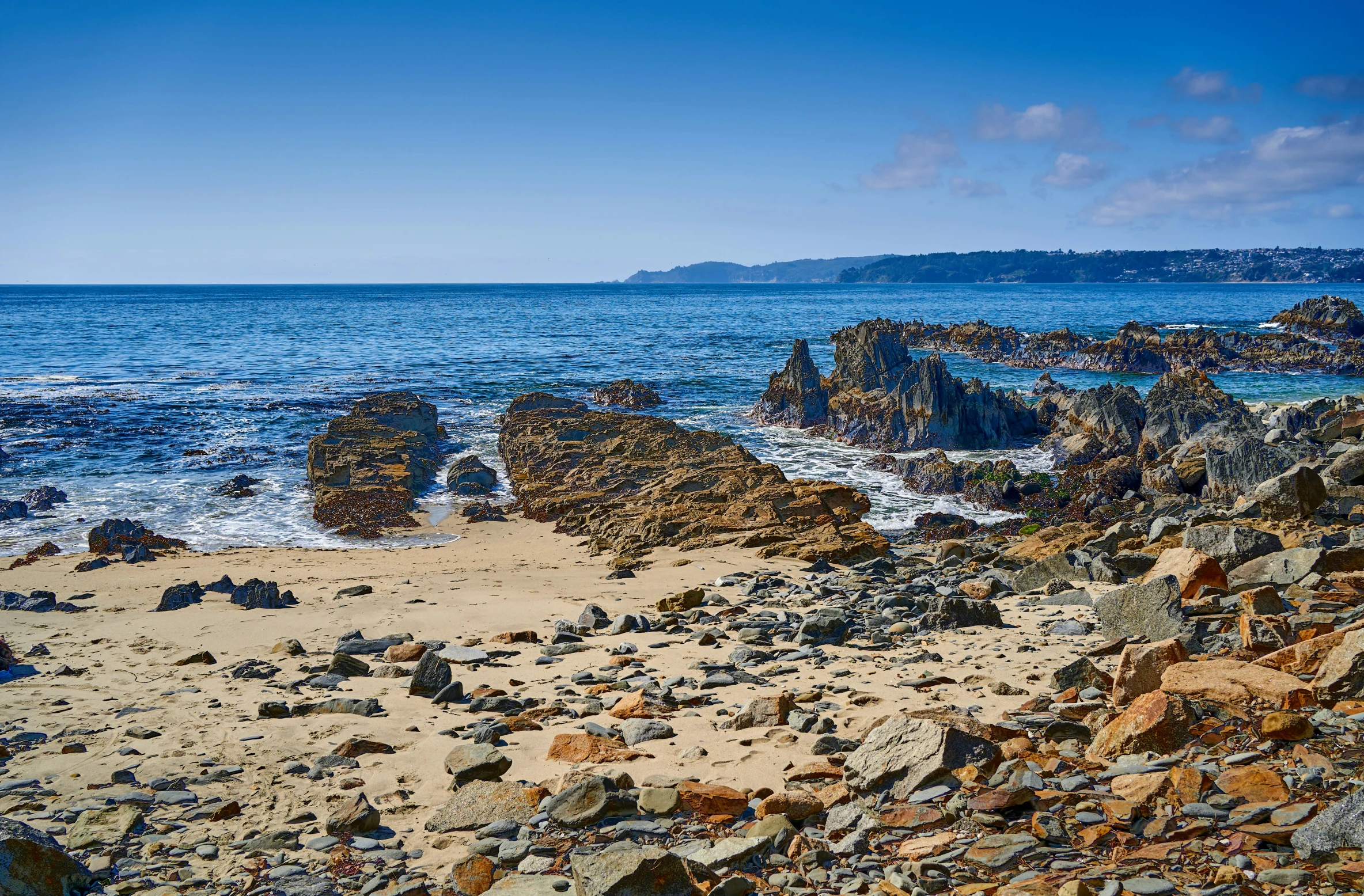 a blue sky and sea near some rocks and the beach