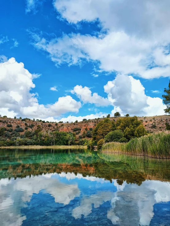 a lake surrounded by green trees with clouds and some blue skies