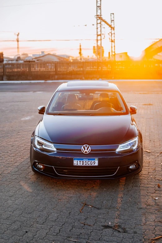 a black car in a parking lot with the sun setting behind it