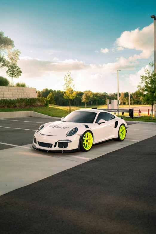 the white porsche parked in a lot with some yellow wheels