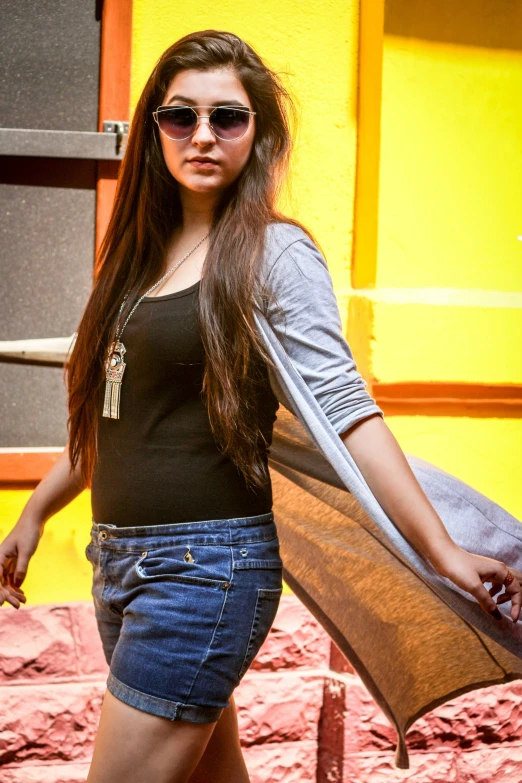 a woman in sunglasses is posing near yellow buildings