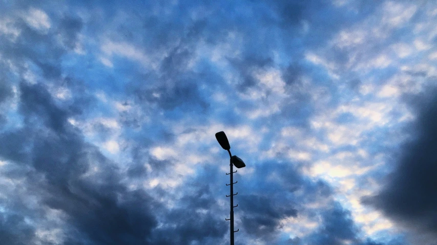 a tall lamp post in front of a blue cloudy sky