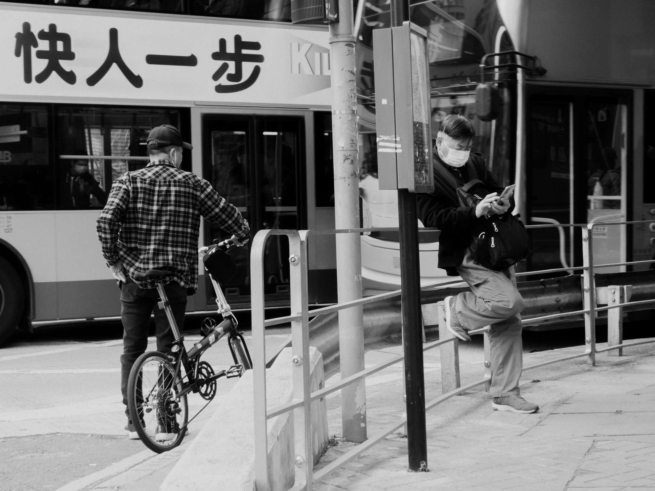 two men are standing outside a bus and looking at their phones