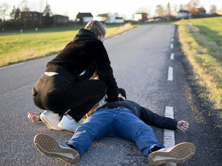 two people, one sitting and one standing, on the street with one laying down