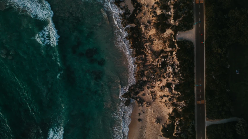 an aerial view of an asphalt road passing through a beach