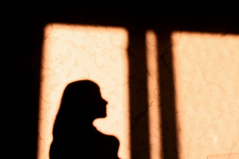 silhouette of woman next to wall with the light coming through the windows