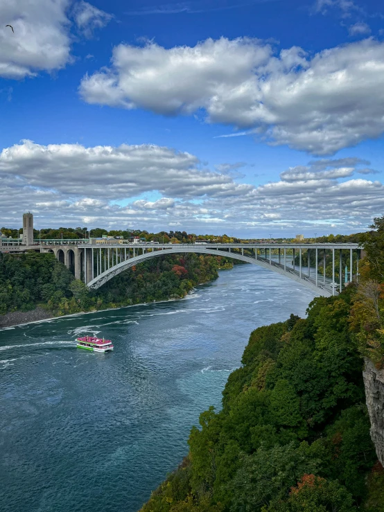 a river below a bridge under a cloudy blue sky