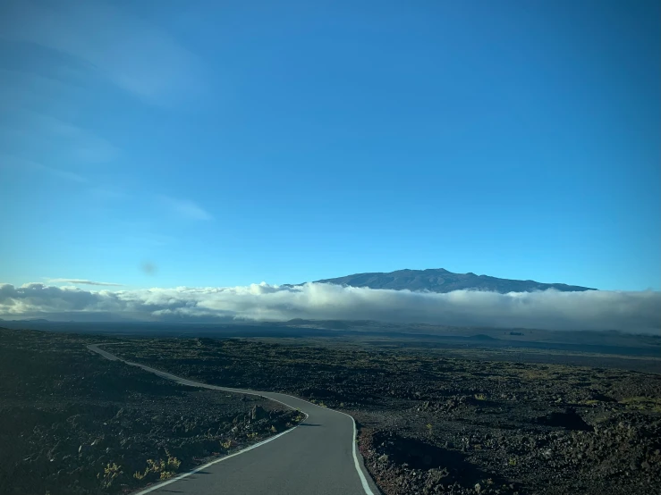 a winding highway is in the desert with low clouds coming up