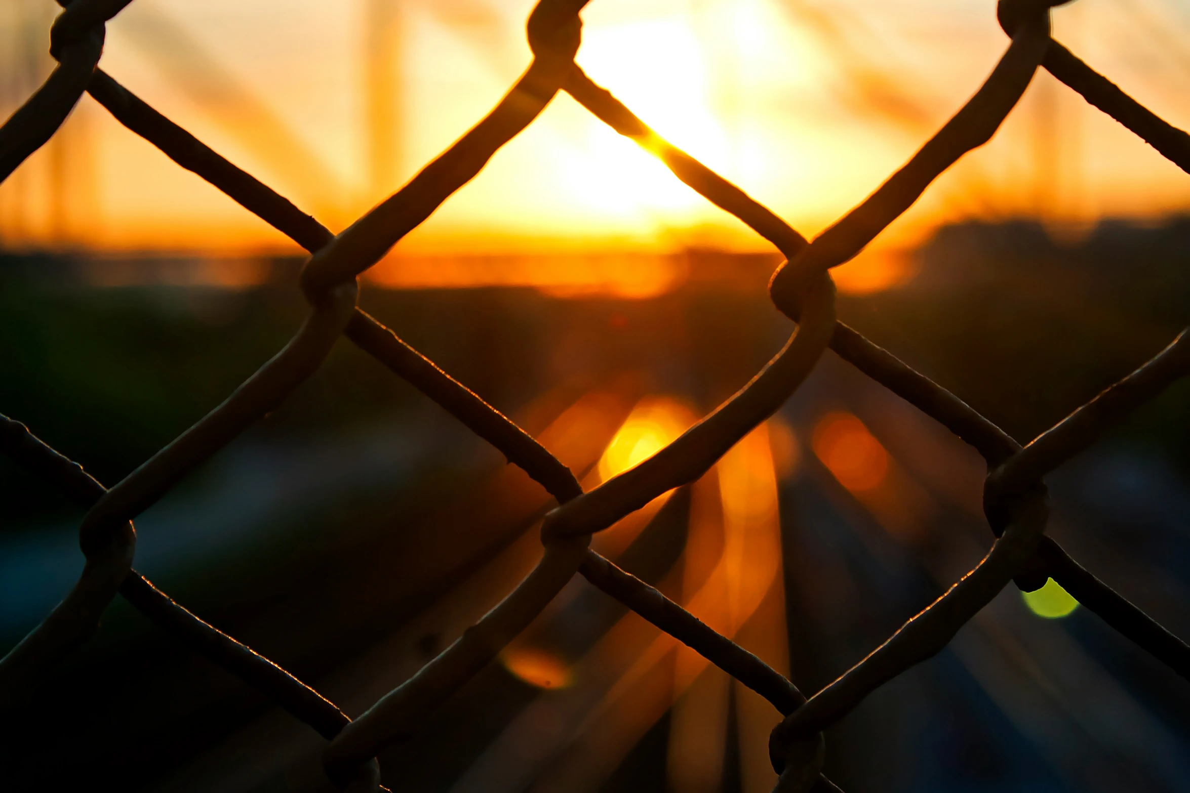 the sun is setting in the background behind a chain link fence