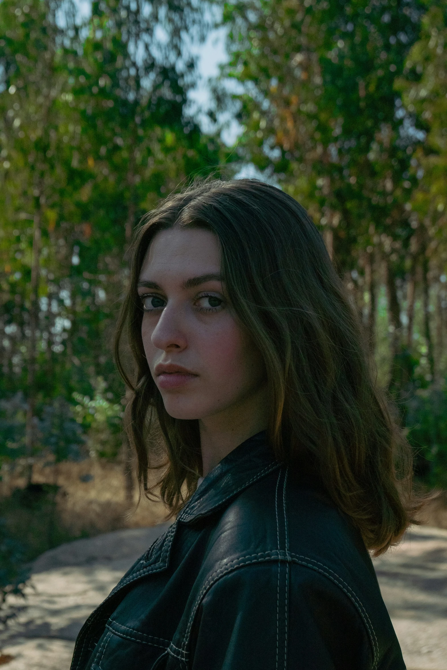 a woman in leather jacket with trees in background