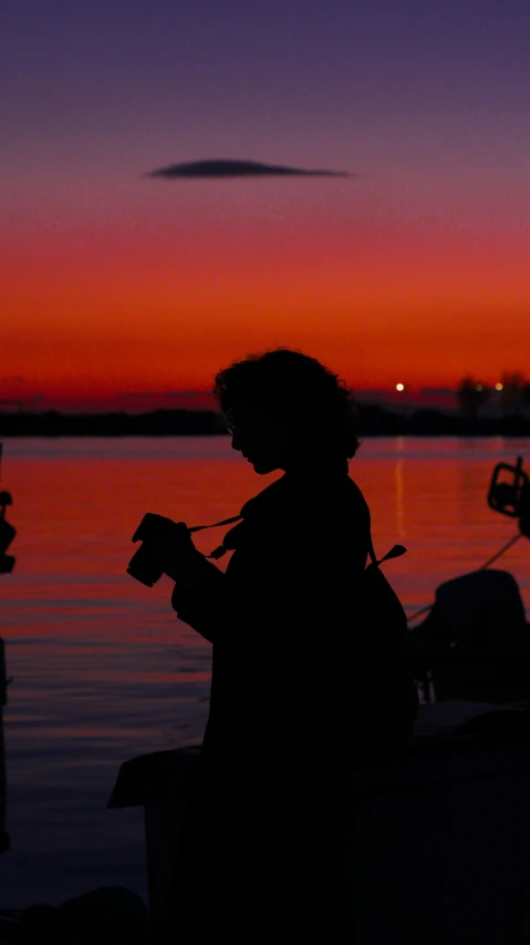 a woman sitting next to the water at dusk with a book