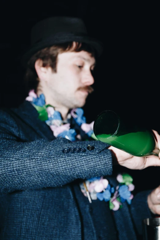 a young man in a suit and hat pouring green liquid into a cup