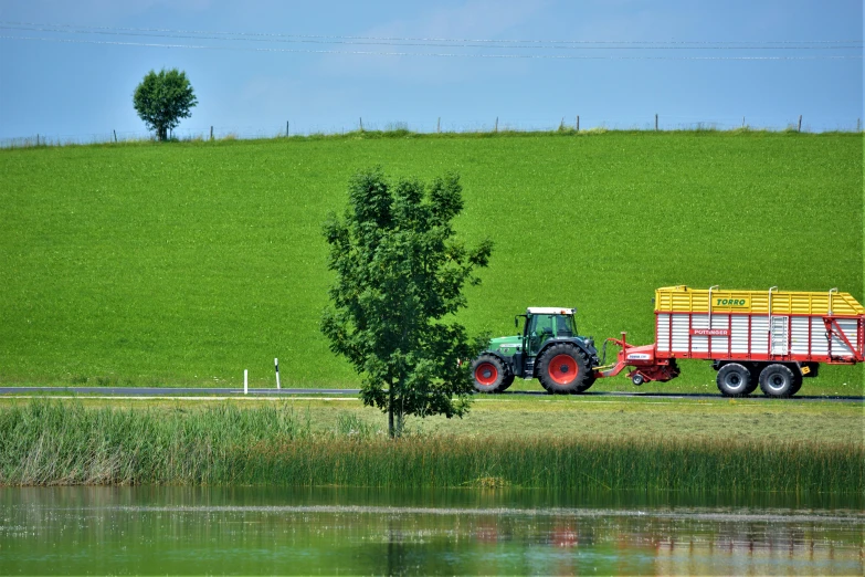 a tractor pulling a trailer beside a pond on a farm