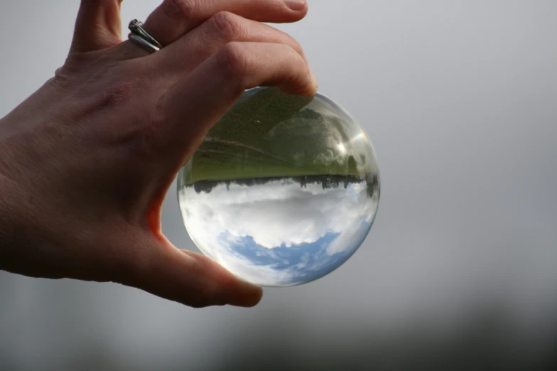 a hand holding an oval, reflecting blue skies in the glass orb