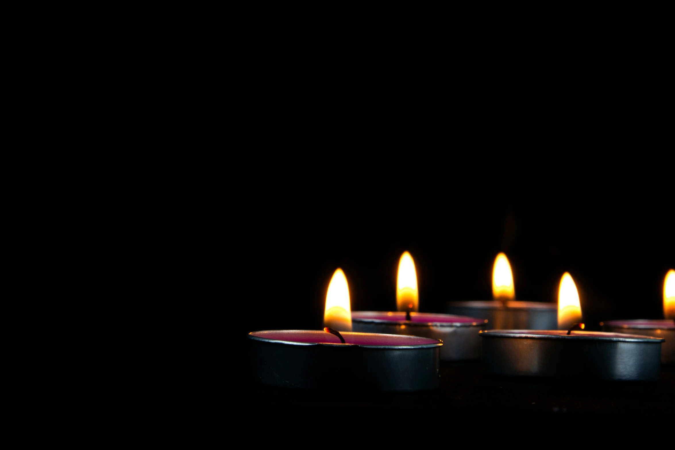 seven lit candles are shown on a dark surface