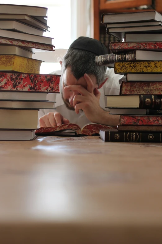 a man leans his head in front of a stack of books