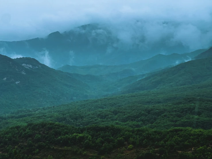 clouds are hovering over the rolling mountains