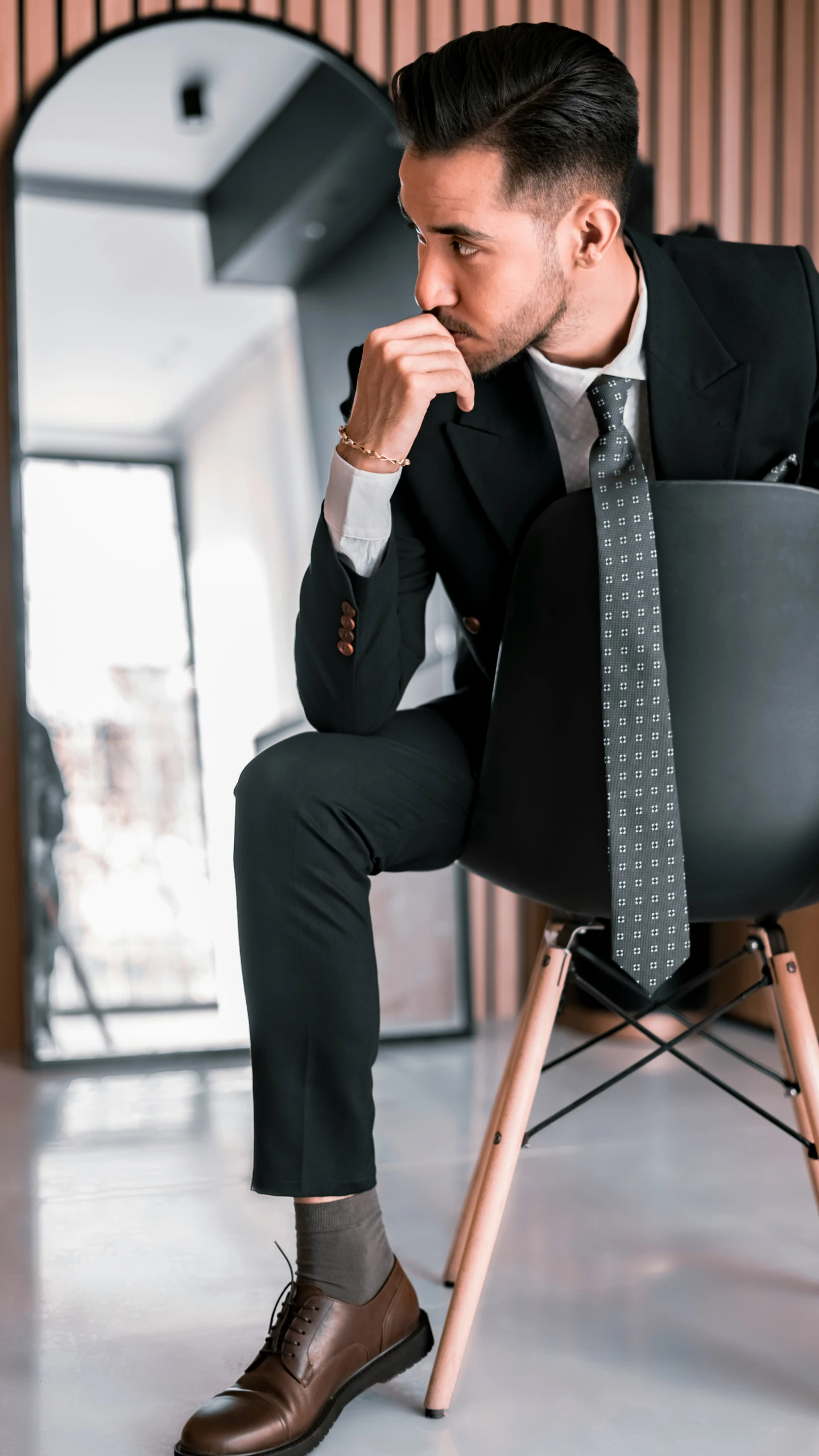 a man in a suit sitting in a chair holding his chin