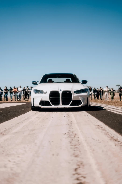 a white sports car driving on dirt road near crowd of people