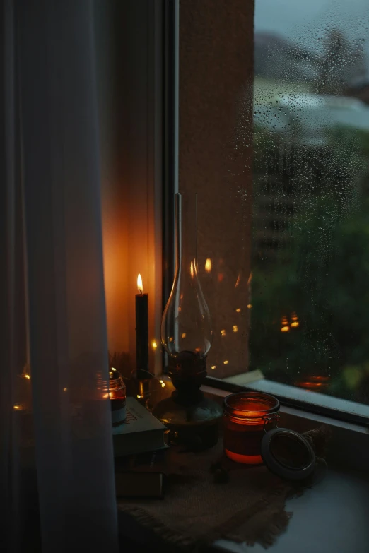 two candles sit near an open window on a rainy day