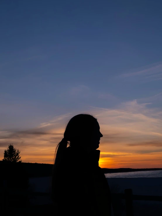 the sun rising behind a silhouetted woman on her cellphone