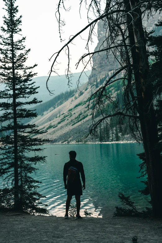 a person is standing on the shore of a mountain lake