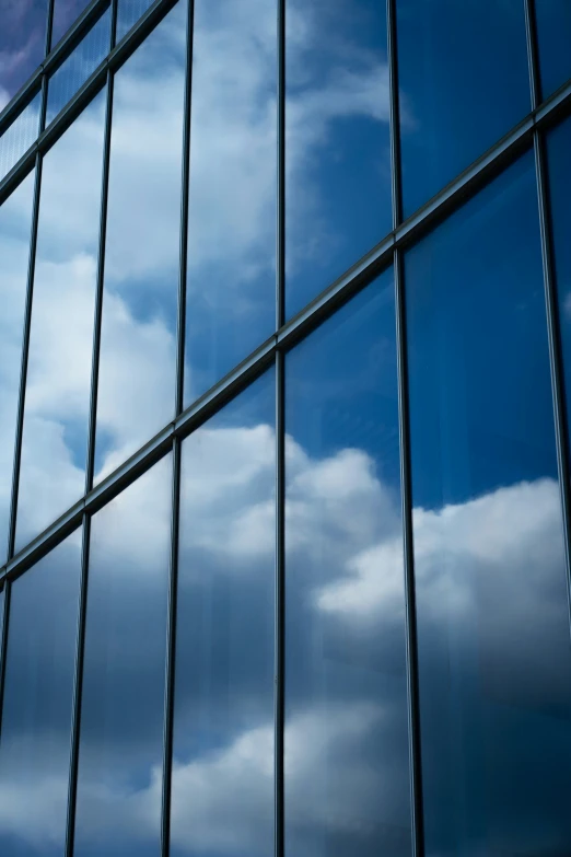 the front of a large building has glass walls that lead to a sky with clouds