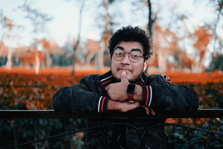 a man with glasses leaning on a fence