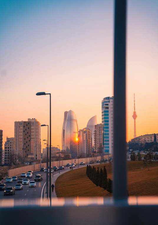 a city street at sunrise in the foreground is tall buildings and some trees