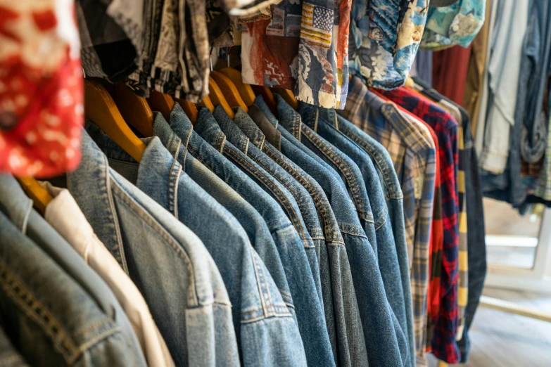 a row of jeans hanging on hangers with shirts on them